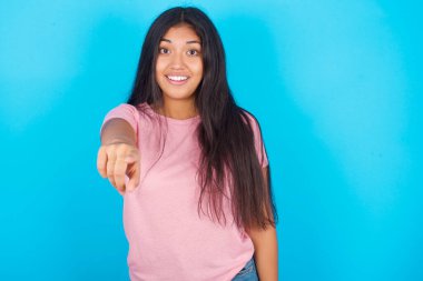 Heyecanlı pozitif kadın işaret parmağıyla seni işaret ediyor ve çok komik bir şey görüyor. Vay canına, inanılmaz. Pembe tişört giyen esmer, güzel bir kadın mavi arka plana poz veriyor.