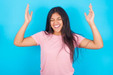  Kadın, korkunç bir durum yüzünden kendini stresli hissederken deliriyor. Pembe tişört giyen esmer, güzel bir kadın mavi arka plana poz veriyor.