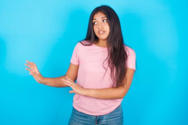 Hoşnutsuz bir kadın ellerini boşluğa uzatır ve yakına gelmemesini ister. Hoş olmayan bir şey görür. Pembe tişört giyen esmer, güzel bir kadın mavi arka plana poz veriyor.