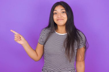 Mor arka plana bakan çizgili tişörtlü, güzel, esmer bir kadın.