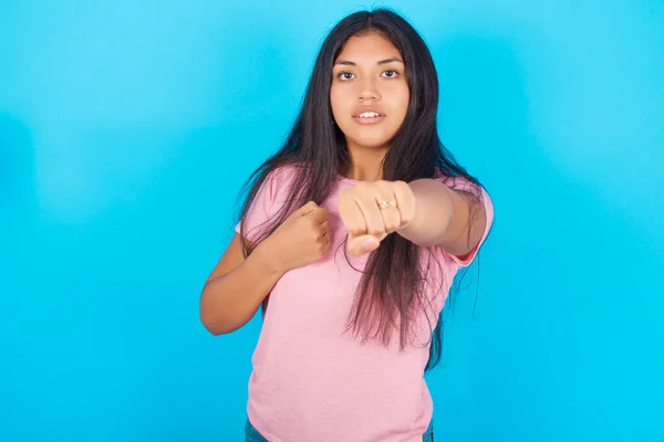 少女拳打脚踢打斗 咄咄逼人和愤怒的攻击 威胁和暴力 年轻美丽的西班牙裔黑发女子 身穿粉色T恤 背景为蓝色 — 图库照片