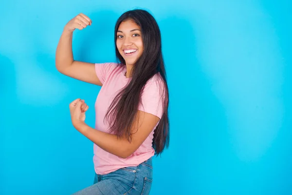 照片上兴奋的女孩举起拳头庆祝黑色星期五购物 年轻美丽的西班牙裔黑发女子 身穿粉色T恤 背景为蓝色 — 图库照片