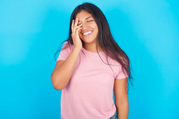 女孩做鬼脸 大大的笑着 笑着肯定听到滑稽的笑话姿势 年轻美丽的西班牙裔黑发女子 身穿粉色T恤 背景为蓝色 — 图库照片