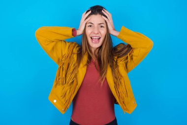 Paniğe kapılmış genç, güzel bir kadın mavi stüdyo arka planında ceket giyiyor, el ele tutuşuyor ve umutsuzluk ve hüsran içinde haykırıyor..