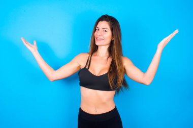 Neşeli, güzel esmer kadın spor giysisi giyiyor. Hoş bir jest yapıyor. Kollarını başının üstüne kaldırıyor..