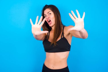 Tatminsiz esmer kadın spor kıyafetleri giyiyor, kaşlarını çatıyor, iğrenç bir ifade takınıyor, dilini gösteriyor, itaatsizlik ediyor, birine sinir oluyor..