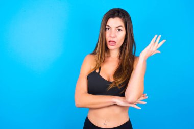 Studio shot of frustrated beautiful brunette woman wearing sportswear gesturing with raised palm, frowning, being displeased and confused with dumb question.