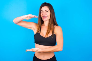 Güzel esmer kadın spor giysisi giyiyor. Elleriyle büyük ve büyük bir işaret veriyor. Ölçü sembolü..