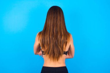 Güzel esmer kadın spor giysisi giyiyor geriye bakıyor kollarını vücuduna dikiyor..