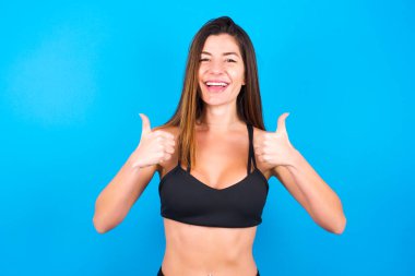 İyimser, güzel esmer kadın spor giysisi giymiş olumlu duygularla başparmağını kaldırıyor. Kalite ve tavsiye kavramı.
