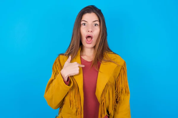 ブルースタジオのバックグラウンドでジャケットを着ている女性は ショックを受け 指で自分自身を指摘する驚くべき表情を持っています — ストック写真