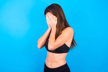 Üzgün, güzel esmer kadın spor kıyafetleri giyiyor, yüzünü ellerle kapatıyor ve ağlıyor..