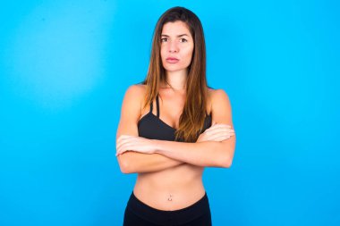 Güzel esmer kadın spor giysisi giyiyor. Yüzünü hoşnutsuzlukla buruşturuyor. Kollarını kavuşturup bir açıklama bekliyor..