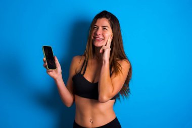 Düşünen güzel esmer bir kadının spor giyim kuşamında cep telefonu kullandığını ve el ele tutuştuğunu hayal et. Karar almak ve sosyal medya kavramı.