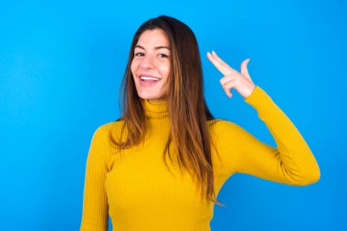 Sarı balıkçı yaka kazak giyen genç bir kadın şakakta parmaklarıyla ateş ederek intihar jesti yapıyor. Parmak tabancası yapan komik bir model.