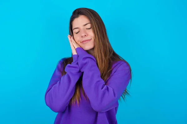 美丽的女人 穿着紫色毛衣 披着蓝色的工作室背景 靠在紧闭的手掌上 闭上眼睛 带着愉快的微笑 梦想着什么 — 图库照片