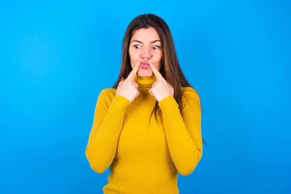 黄色のタートルネックセーターを着て 目を交差させ 魚の唇を面白いグリムを作る若い女性 — ストック写真