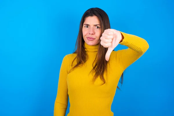黄色のタートルネックセーターを着た若い女性は 不幸で怒って 親指のジェスチャーで拒絶と否定を示しています バッド表現 — ストック写真