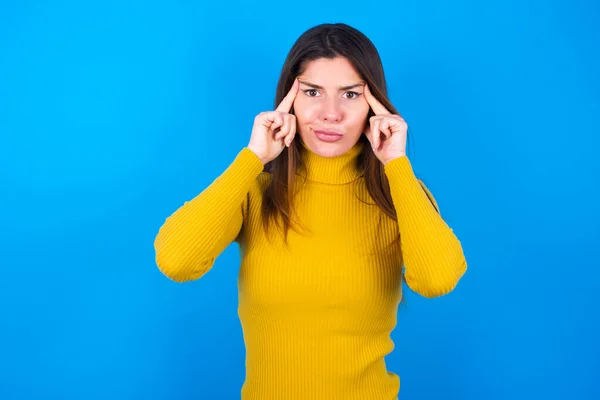 寺院に指を置き 緊張を和らげ 思考を集め 試験のための重要な情報を覚えようとする黄色いタートルネックセーターを身に着けている真剣に濃縮された若い女性 — ストック写真
