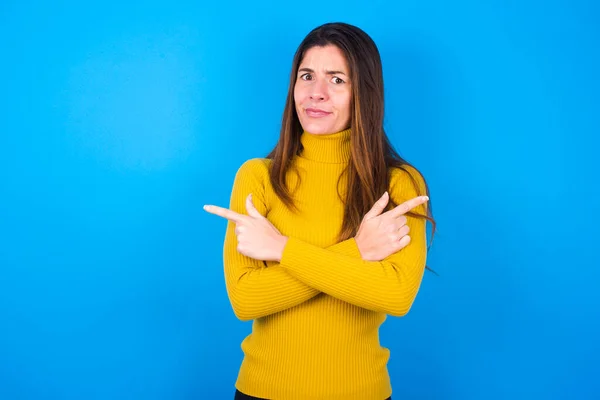 严肃的年轻女人穿着黄色的高领毛衣 手牵着手 指着不同的侧面 在两件衣服之间踌躇着 硬性决策概念 — 图库照片