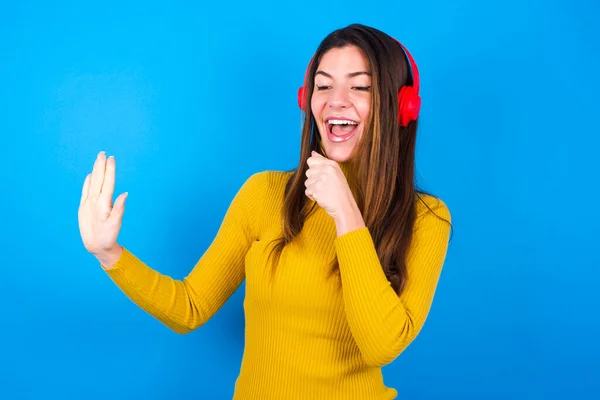 お気に入りの歌を歌う幸せな女性は ワイヤレスヘッドフォンを着て音楽を聴いているかのように 手の近くに手を保つ — ストック写真