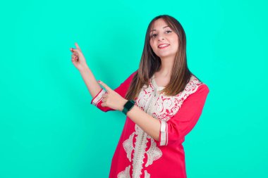 Genç, beyaz, güzel bir kadın boş bir yeri işaret ediyor. En düşük fiyatları gösteriyor. Kameraya bakıyor.