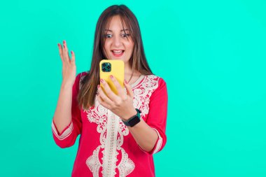 Genç, güzel, beyaz bir kadın elinde akıllı bir telefon tutuyor ve haberleri okuyor.