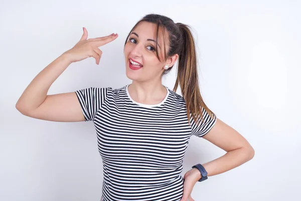 Stüdyoda beyaz arka planda silah hareketi gösteren çizgili tişört giyen genç bir Arap kadın. 