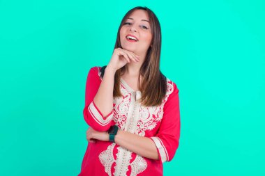 İyimser, genç, beyaz, güzel bir kadın ellerini kısmen çapraz tutuyor ve elleri çenesinin altında kameraya zevkle bakıyor. Mutlu duygu konsepti.