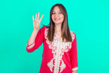 Genç, güzel, beyaz bir kadın kendini beğenmiş ve mutlu bir şekilde gülümserken dört numarayı gösterip işaret ediyor..