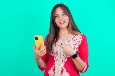 Genç, güzel, beyaz bir kadın el ele tutuşup yeni bir akıllı telefon gösteriyor. 