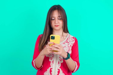 Heyecanlı genç beyaz kadın göz kırpıyor ve elinde akıllı bir telefonla sosyal ağ haberleri okuyor.