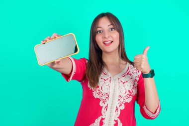 Portre genç, beyaz bir kadın elinde akıllı bir telefonla baş parmağını gösteriyor.