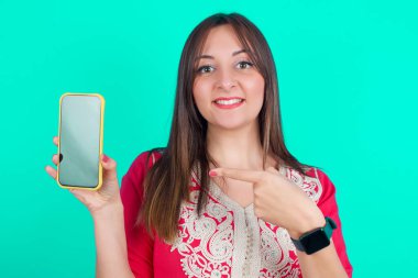 Gülümseyen güzel beyaz kadın boş ekranla cep telefonunu işaret ediyor.