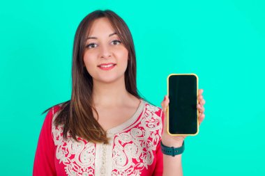 Gülümseyen genç beyaz kadın boş ekranlı cep telefonunu tutuyor.