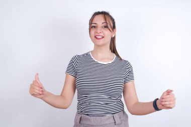 Beyaz arkaplan üzerine çizgili tişört giyen mutlu genç Arap kadın. Boş Kağıt Tahta İlan Bülteni Metni Duruşu. Sonbahar Reklam Afişi.