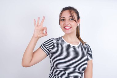 Genç, beyaz bir kadın tişört giyiyor, el ele tutuşuyor. Tamam, dişlek, yeni haberleri onaylıyor.