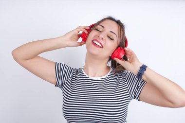 Tişört giyen güzel beyaz kadın gülümseyerek en sevdiği müziği kablosuz kulaklıkla dinlediği için çok mutlu..