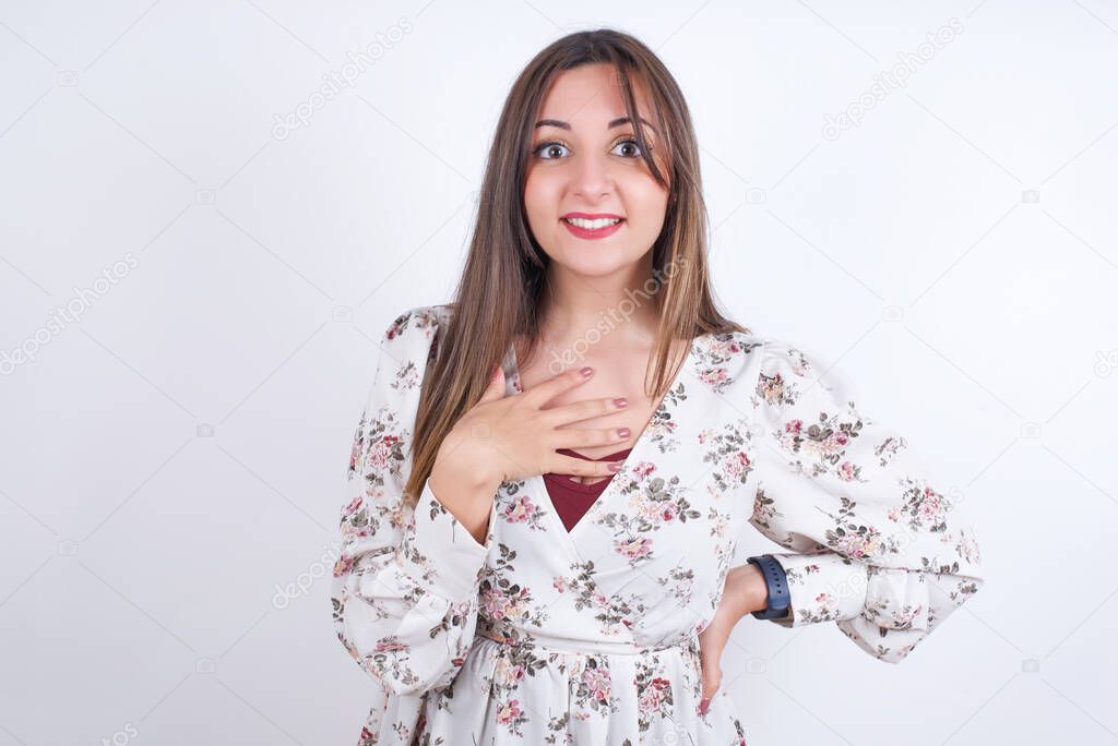 woman wearing floral dress over white background smiles toothily cannot believe eyes expresses good emotions and surprisement