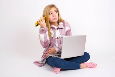 Gülümseyen, beyaz arka planda dizüstü bilgisayarı olan beyaz saçlı güzel bir kız akıllı telefonundan gelen sesli mesajı dinliyor. İletişim ve teknoloji kavramı.