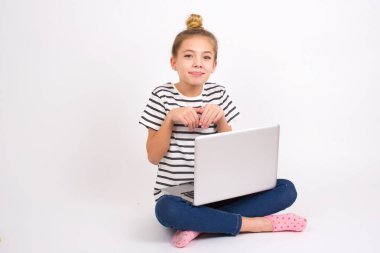 Beyaz arka planda Lotus pozisyonunda dizüstü bilgisayarı olan beyaz saçlı güzel bir genç kız tavşan pençeleri yapıyor ve masum bir ifadeyle küçük çocuğuyla oynuyor.