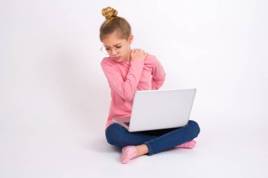 Beyaz arka planda dizüstü bilgisayarı olan beyaz saçlı güzel bir genç kız sırt ağrısı çekiyor.