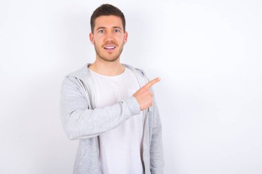 Beyaz arka plan üzerine günlük giysiler giymiş genç beyaz bir adam sana gülümsüyor. Şuraya bak.!