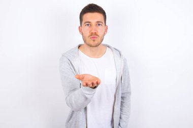 Beyaz arka plan üzerine gündelik giysiler giymiş genç beyaz bir adam kameraya bakıyor ve havada el ele öpüşme çok güzel oluyor. Aşk ifadesi.