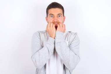 Endişe - beyaz arka plan üzerine günlük giysiler giyen genç beyaz bir adam ellerini bir şeyden ya da biri tarafından ısırılmaktan korkarak ağzını kapatıyor..