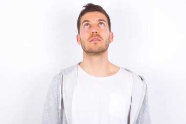 Beyaz arka plan üzerine günlük giysiler giyen genç beyaz bir adam tuhaf bir şey gördüğünde kafasını kaldırdı..