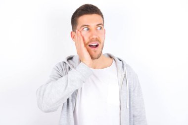 Beyaz arka plan üzerine günlük giysiler giymiş genç beyaz bir adam heyecanla yüzüne bakıyor. Reklam ve şaşkınlık konsepti.