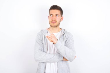 Beyaz arka plan üzerine günlük giysiler giymiş genç beyaz bir adamın portresi. Kamera önünde hileli bir bakışla poz veriyor. Ürünü işaret parmağıyla sunuyor. Reklam kavramı.