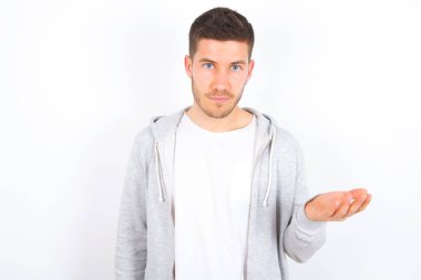 Studio shot of frustrated young caucasian man wearing casual clothes over white background gesturing with raised palm, frowning, being displeased and confused with dumb question.