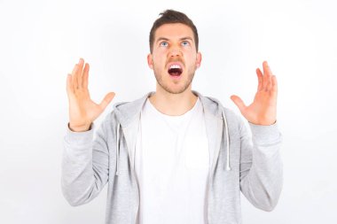 Beyaz arka plan üzerine günlük giysiler giymiş ağlayan ve çığlık atan genç beyaz bir adam. İnsani duygular, yüz ifadesi kavramı. Çığlık, nefret, öfke.